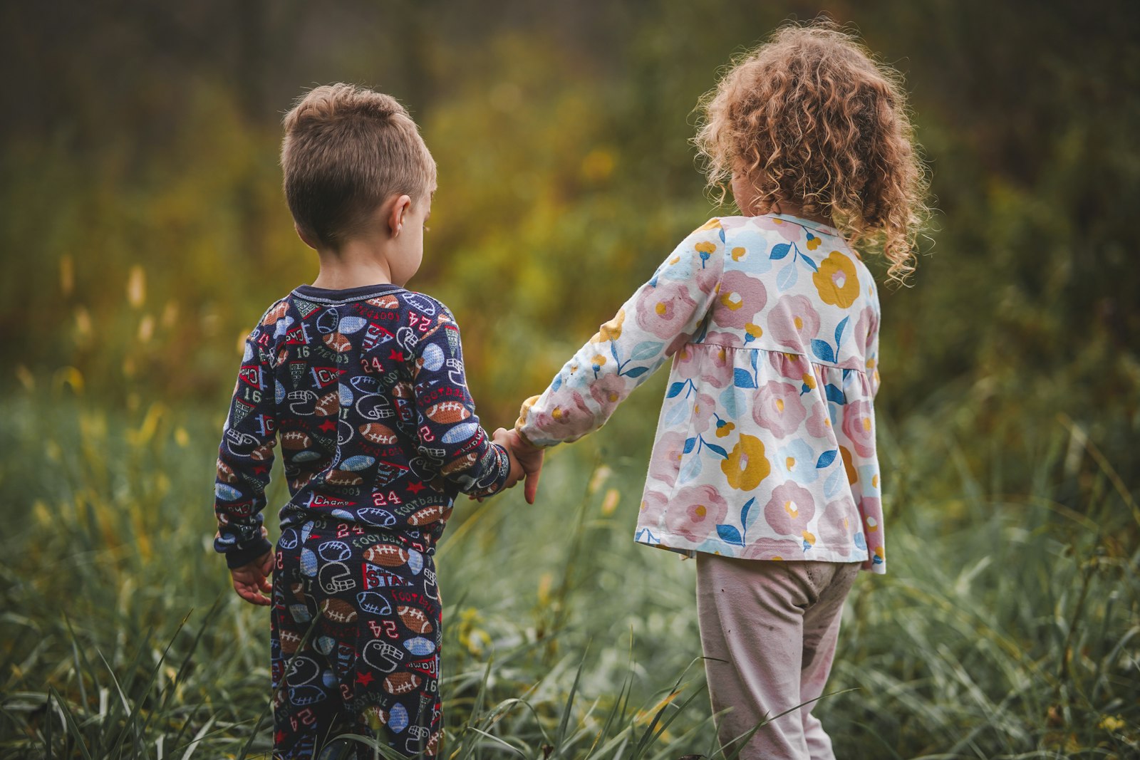 Two children holding hands in a field of tall grass